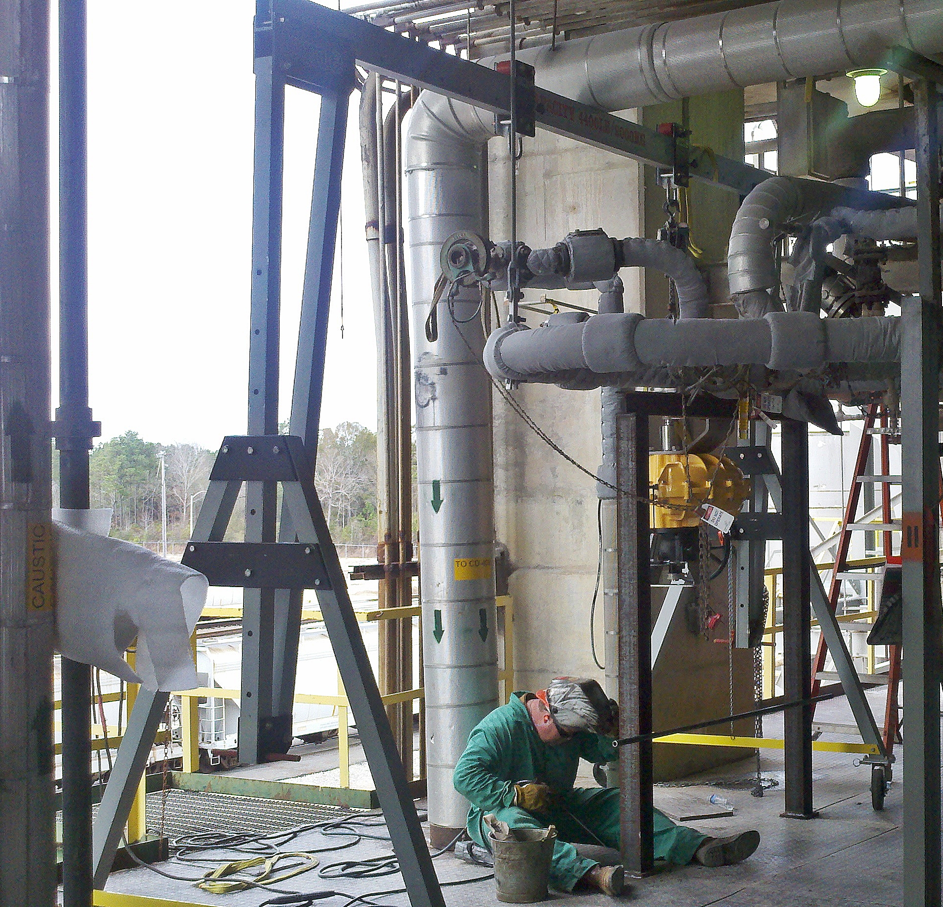 A 4400T aluminum gantry crane positioned among piping in a chemical plant, with a worker performing a valve lift below it.