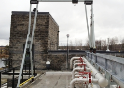 an industrial gantry crane above a series of red and white pipes near a stone building